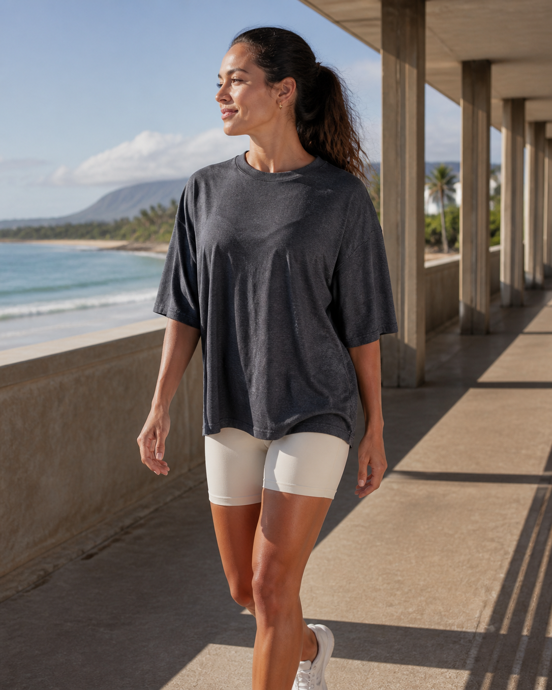 Woman wearing the KeAloha Charcoal rPET Oversized Tee at a coastal pavilion