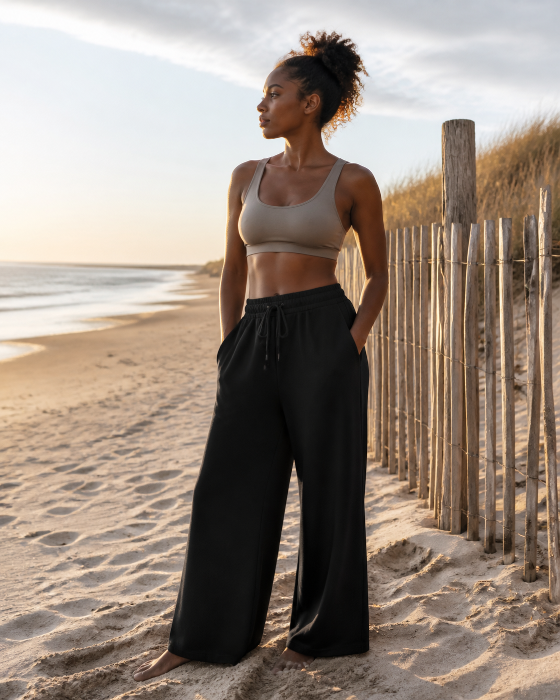 Black Athflow Pants worn on a beach beside dune fencing