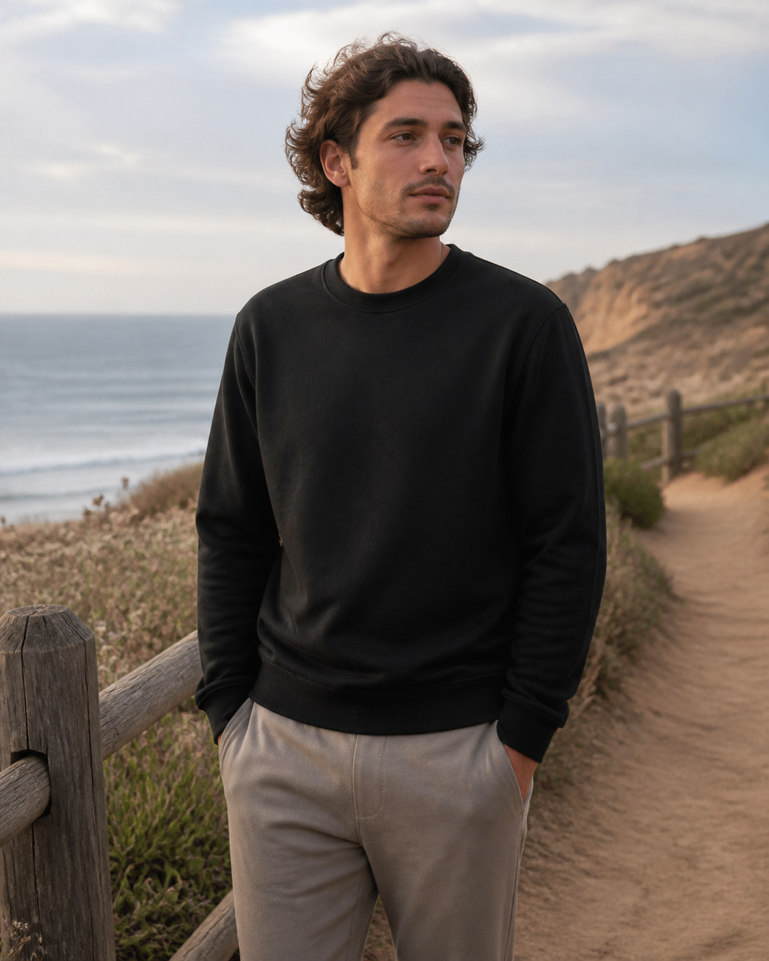 Model wearing KeAloha Black Crewneck Sweatshirt on a coastal trail