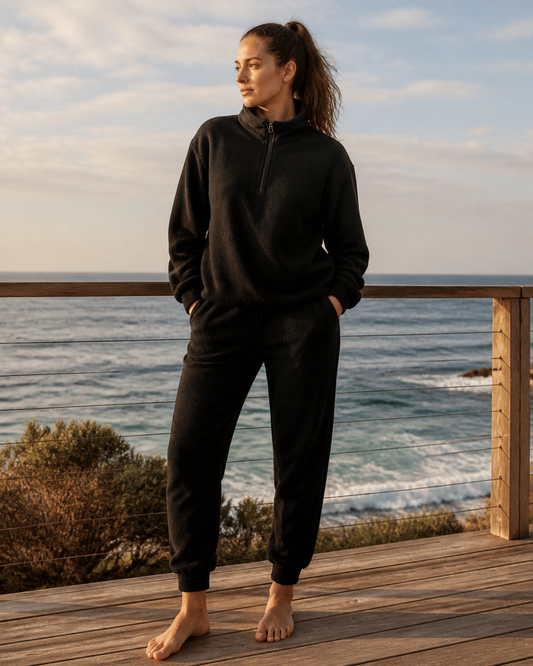 Woman wearing the KeAloha Black Fleece Tracksuit on a coastal boardwalk