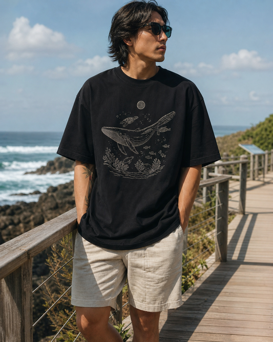 Model wearing KeAloha Black Graphic Oversized Tee on a coastal boardwalk