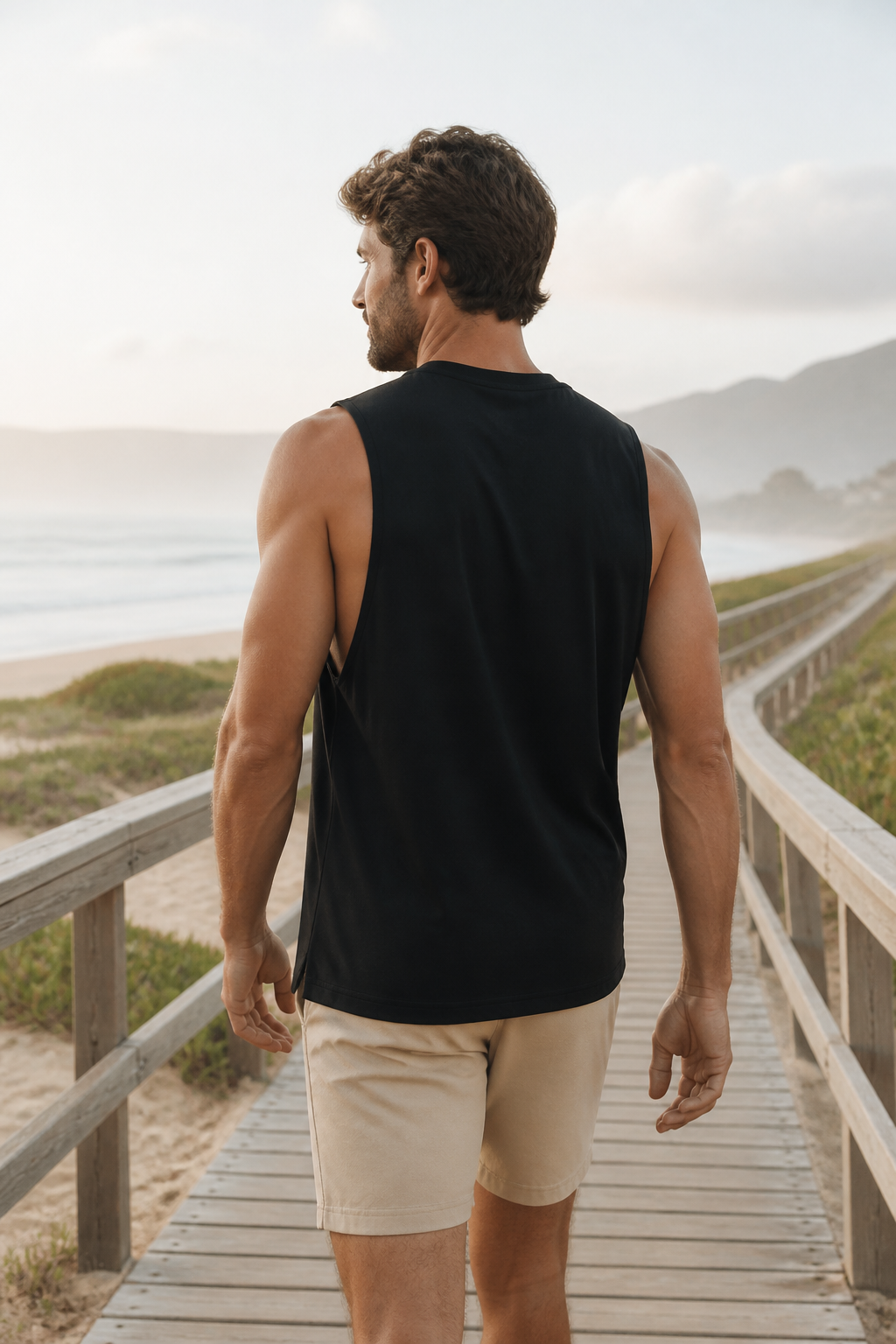 Black loose-fit organic cotton muscle tank back view on a coastal boardwalk
