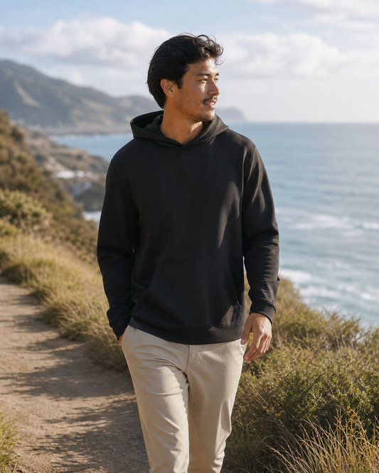 Model wearing KeAloha Black rPET Pullover Hoodie on a coastal trail