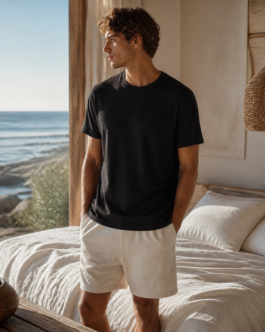Man wearing the KeAloha Black Sleep Tee in a sunlit coastal bedroom