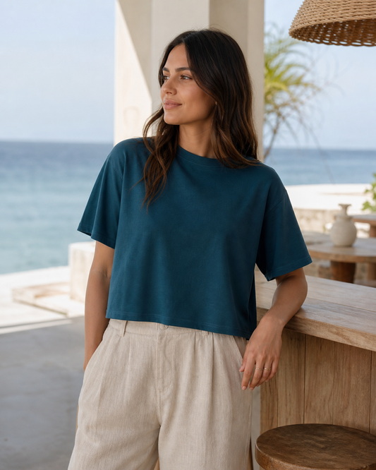 Deep teal organic cotton boxy crop top on an oceanfront terrace