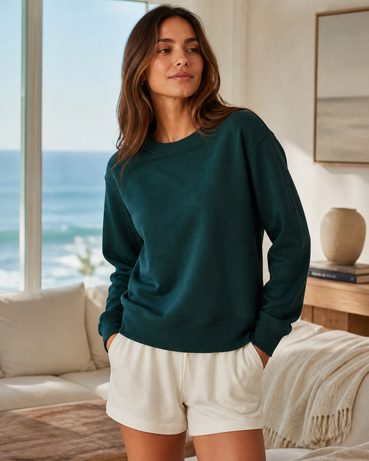 Deep teal organic cotton lounge crewneck in an ocean-view living room