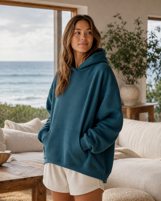 Deep teal oversized lounge hoodie in an ocean-view living room