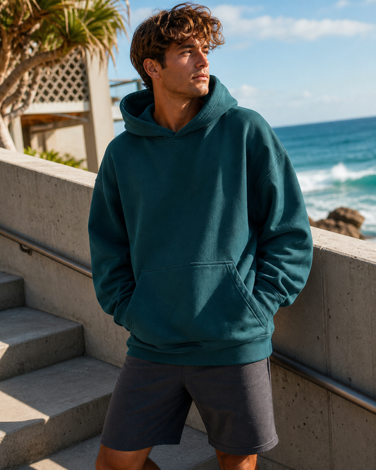 Deep teal oversized pullover hoodie on coastal concrete steps
