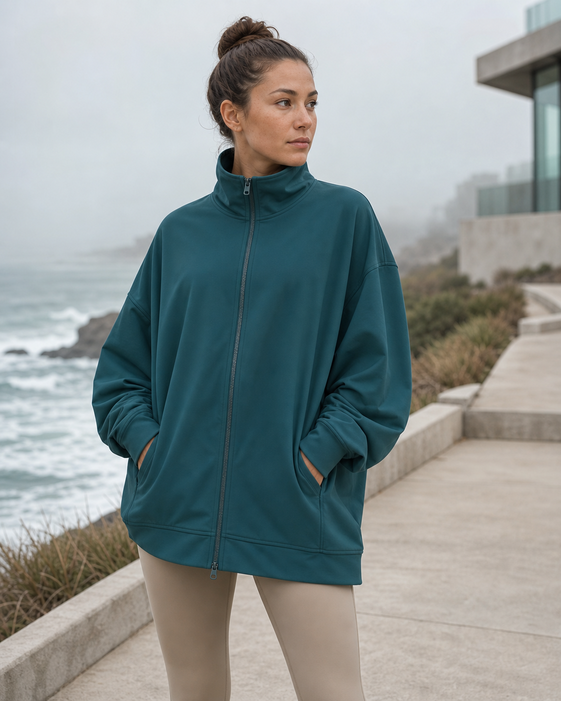 Deep teal oversized recycled track jacket on a foggy oceanfront walkway