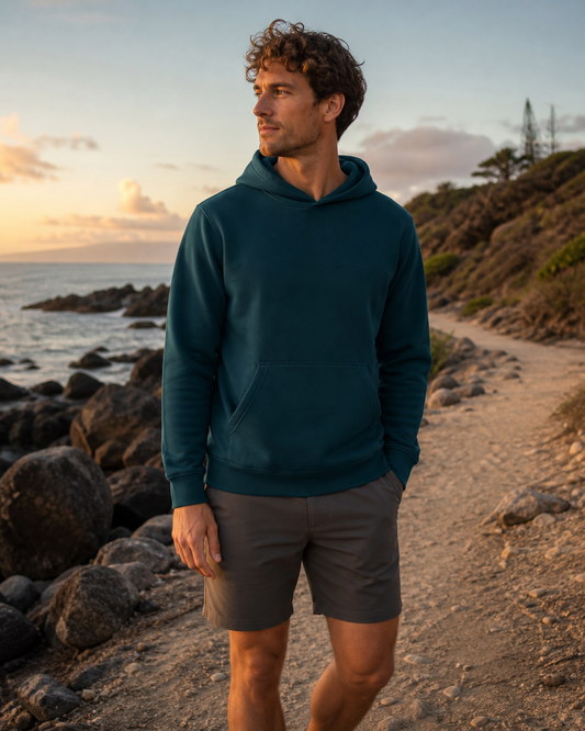 Deep teal standard-fit pullover hoodie on a rocky shoreline path