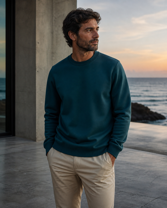 Deep teal recycled-fabric crewneck on an oceanfront terrace