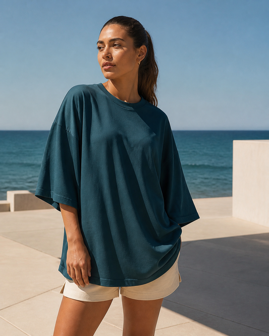 Deep teal recycled-fabric oversized tee on a coastal plaza