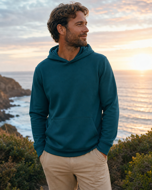 Deep teal recycled-fabric pullover hoodie at sunset by the ocean