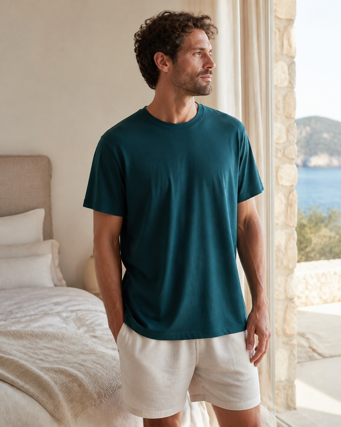 Man wearing a relaxed deep teal organic cotton sleep tee in a coastal bedroom