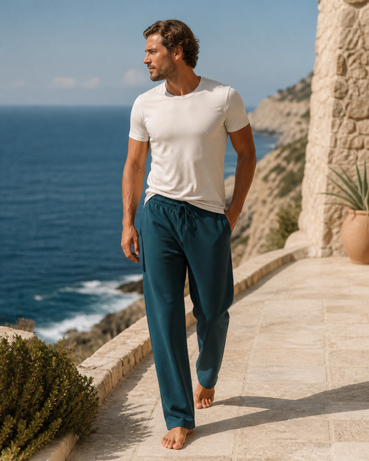 Man wearing deep teal straight-leg organic cotton sweatpants on a coastal terrace