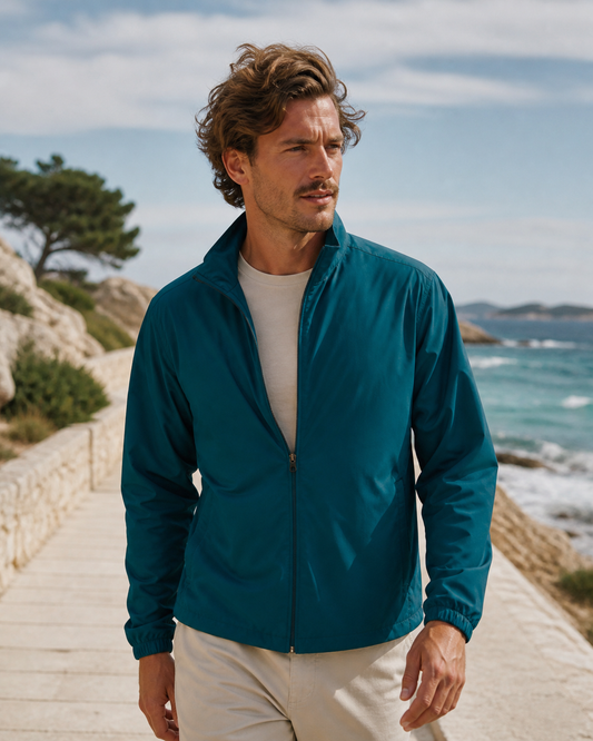 Man wearing a deep teal recycled-fabric track jacket on a coastal boardwalk