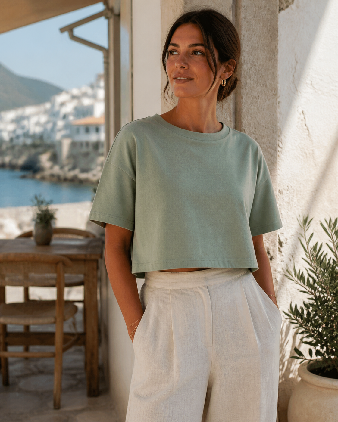Woman wearing a relaxed sage organic cotton boxy crop top at a seaside café