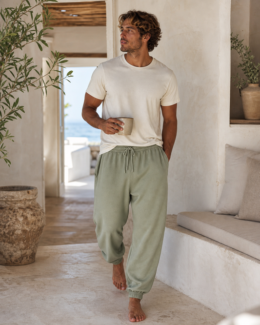 Man wearing oversized sage organic cotton joggers in a coastal home