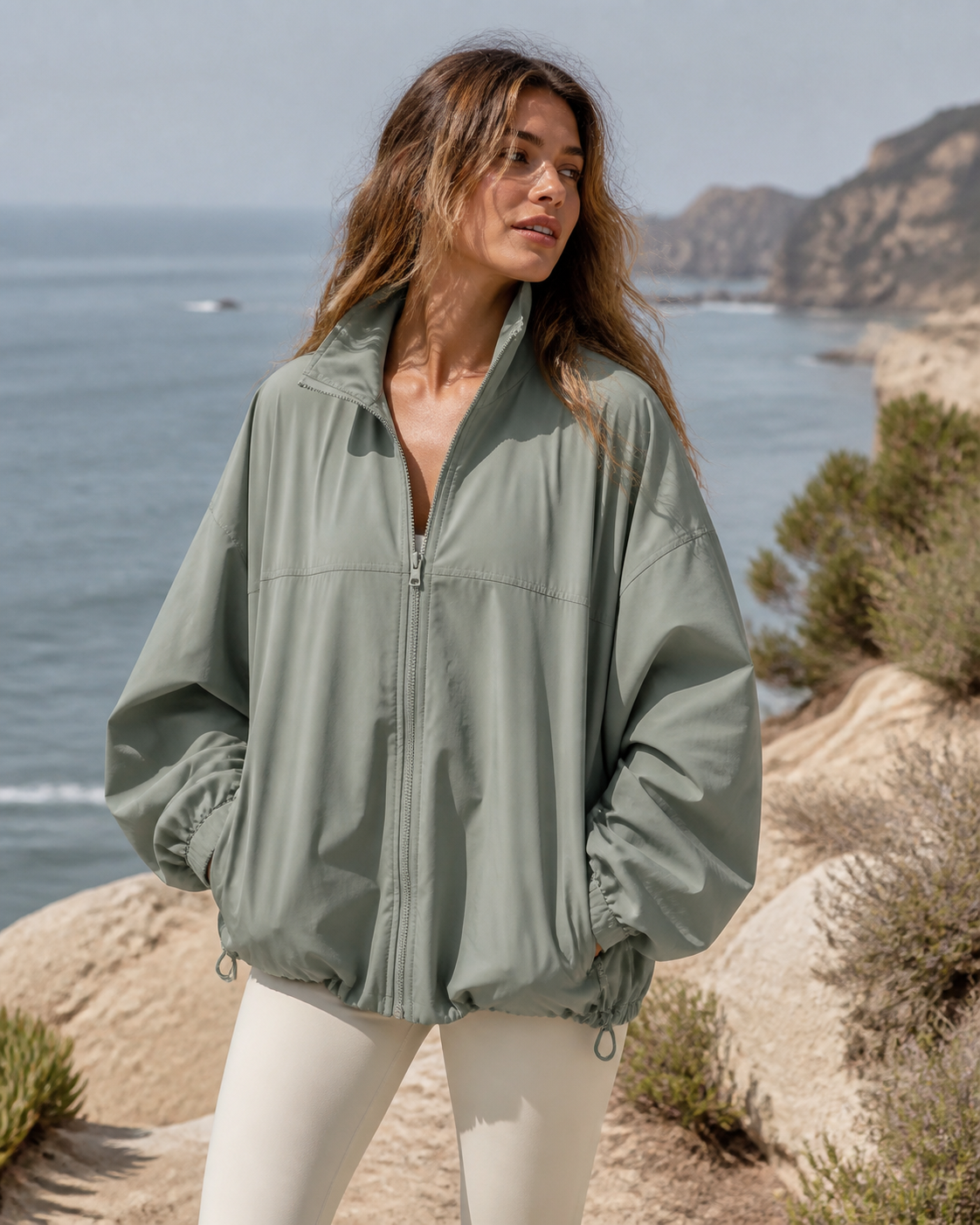 Woman wearing an oversized sage recycled track jacket on a coastal overlook