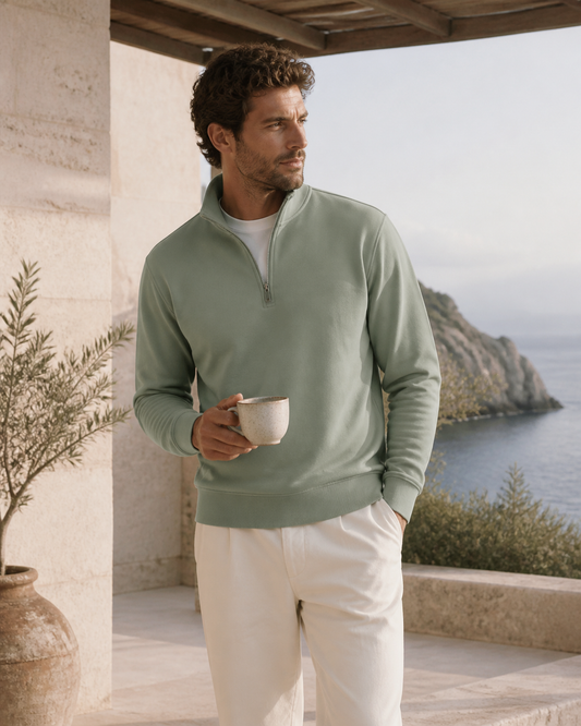 Man wearing a sage organic cotton quarter-zip pullover on a coastal terrace
