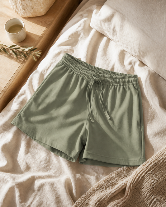 Sage organic cotton sleep shorts arranged on natural linen bedding