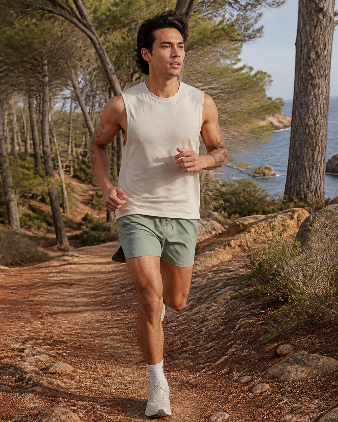 Man running in sage organic cotton split-hem running shorts on a wooded coastal trail