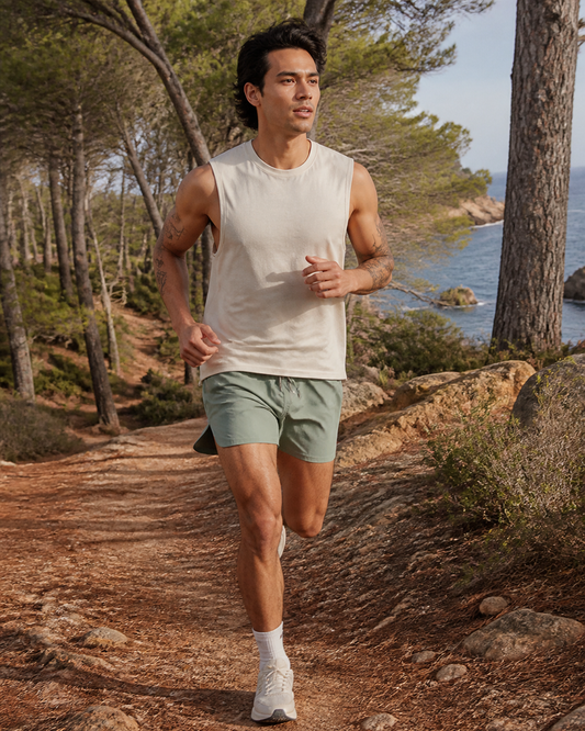 Man running in sage organic cotton split-hem running shorts on a wooded coastal trail