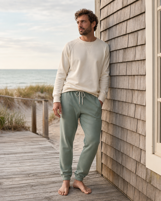 Man wearing sage organic cotton sweatpants with pockets beside a coastal beach house