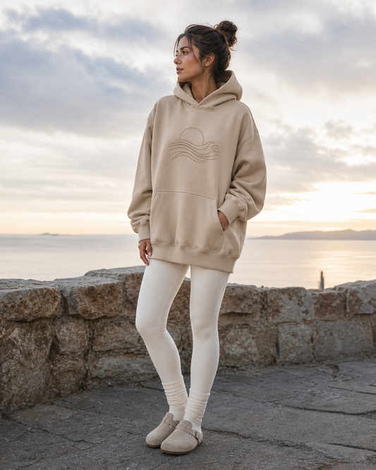 Woman wearing a sand graphic pullover hoodie at a quiet coastal sunrise lookout