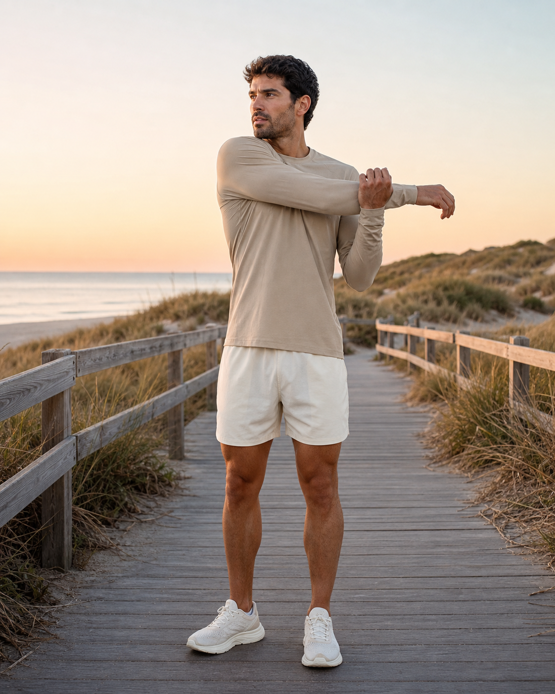 Man stretching in a sand long sleeve training tee on a coastal dune boardwalk