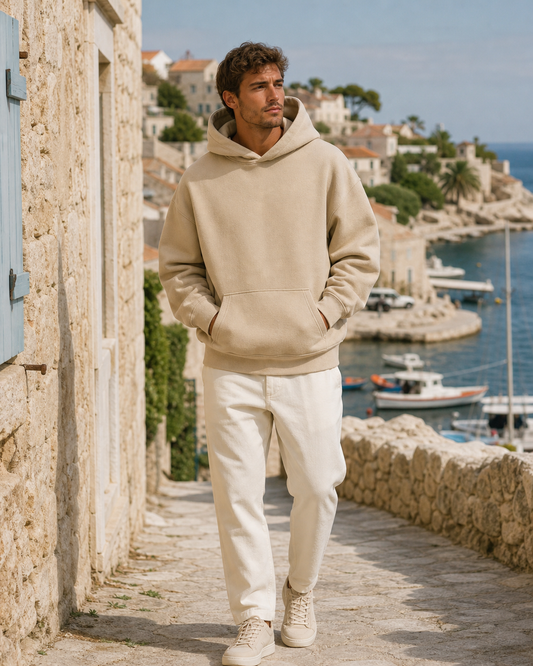 Man wearing a sand oversized pullover hoodie on a coastal village lane above the harbor