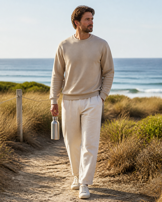 Man wearing a sand recycled-polyester crewneck on a breezy coastal conservation path